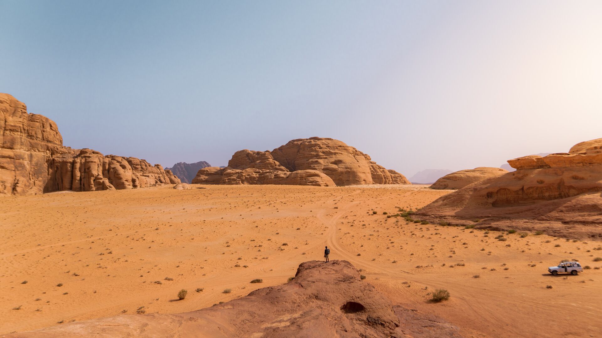 A traveller stands on an outcrop in the distance, overlooking vast swathes of Wadi Rum, Jordan
