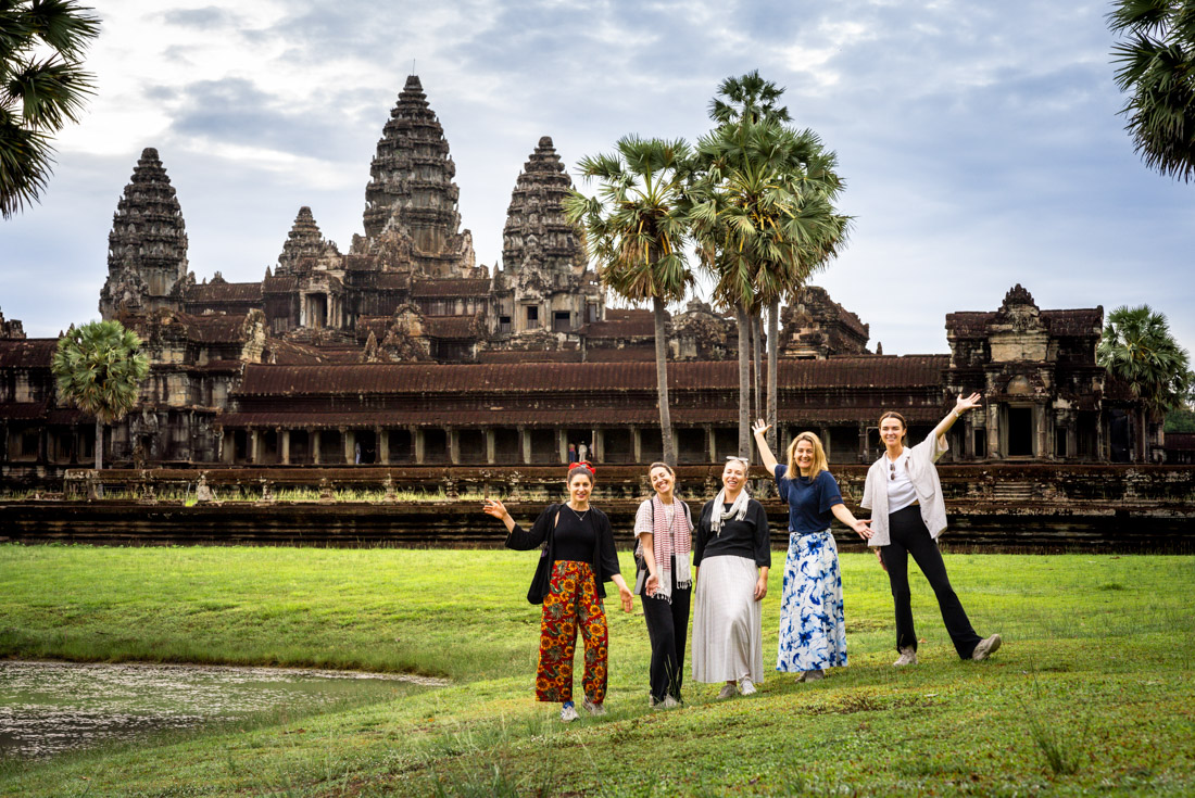 Group of travellers pose happily in front of the Angkor Wat complex at sunrise in Cambodia