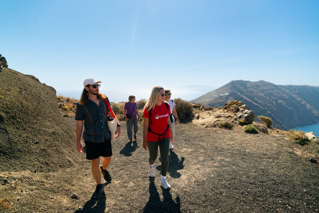 Intrepid leader and travellers hike the caldera ridge of Santorini with mountains visible beyond