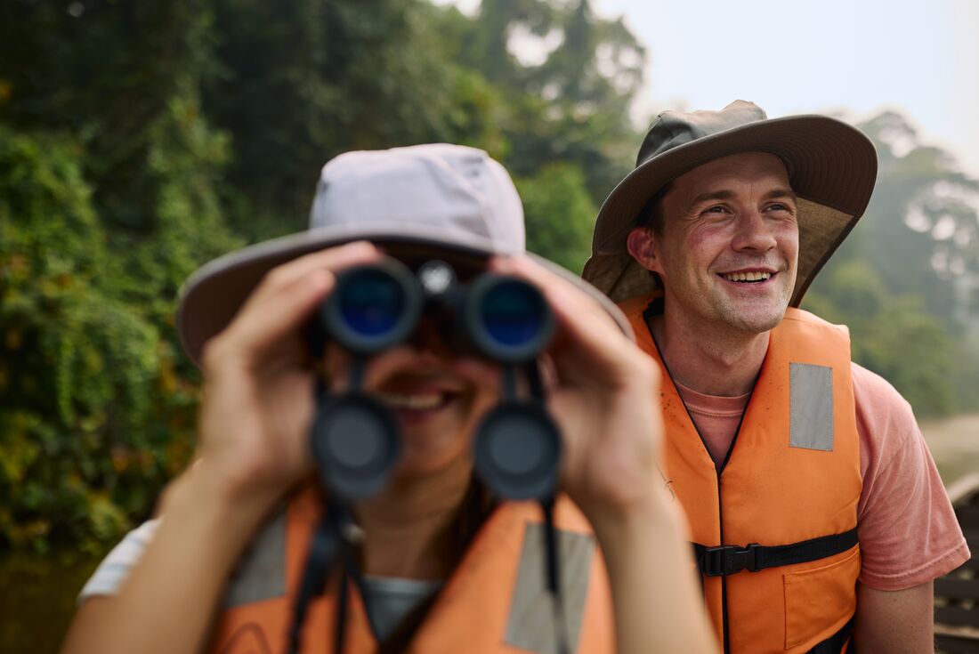 Intrepid traveller looks through binoculars for wildlife on the Amazon river in Peru