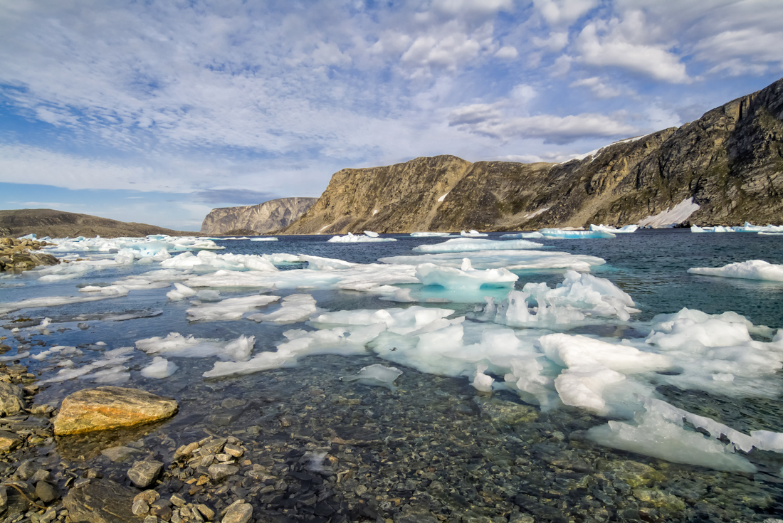 Wide landscape view of Cape Mercy Glacial Fjord with small icerbegs in the bay and rocky mountains beyond
