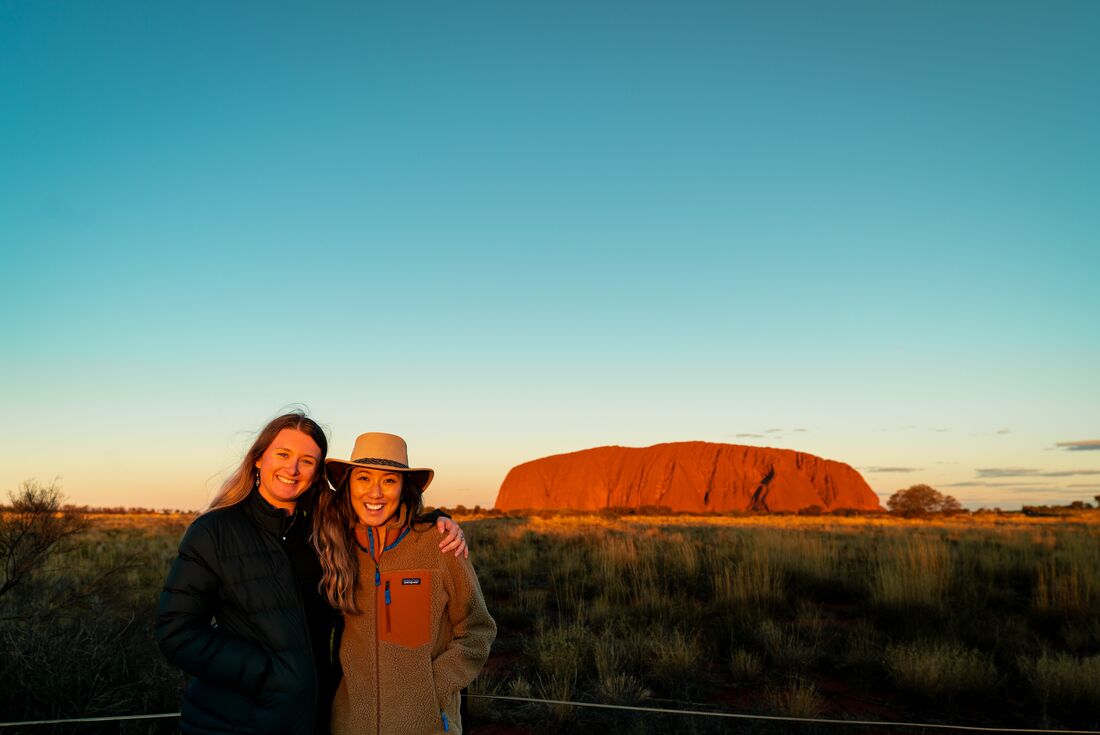 Intrepid travellers pose for a happy photo with Uluru hit by the sunset beyond