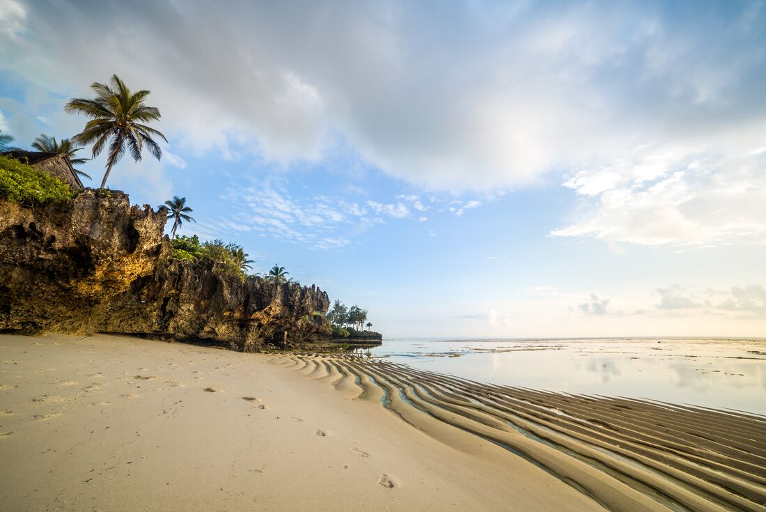 Wave rippled sand on Diani beach at sunset with palms and forest on the edge in Kenya