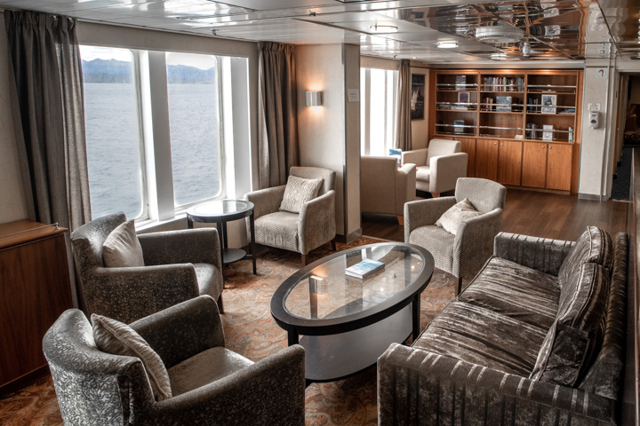 Interior of Compas Club lounge area with tables and seating and a library at the back