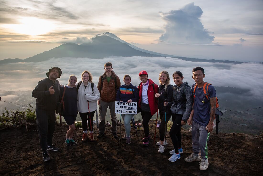 Travellers pose for a photo at the lookout of the Mount Batur Sunrise Hike with morning mist and distant mountains in the background in Bali
