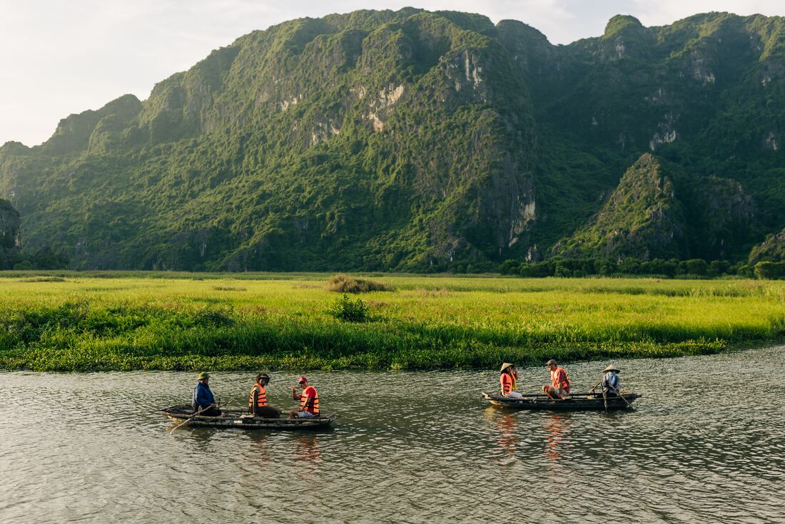 Wide shot of travellers and leader being guided on rowboats in the wide river valley of Van Long Nature Reserve