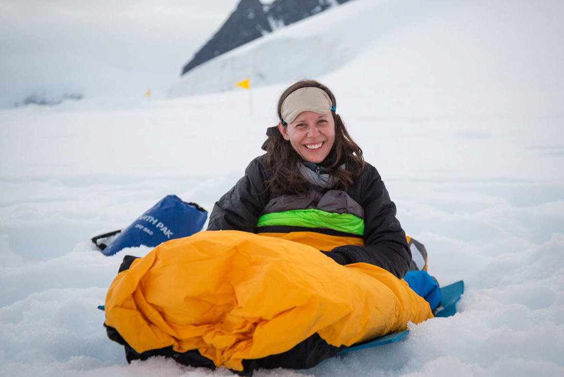 Traveller smiles at the camera while waking up in a bivvy bag after overnight camping