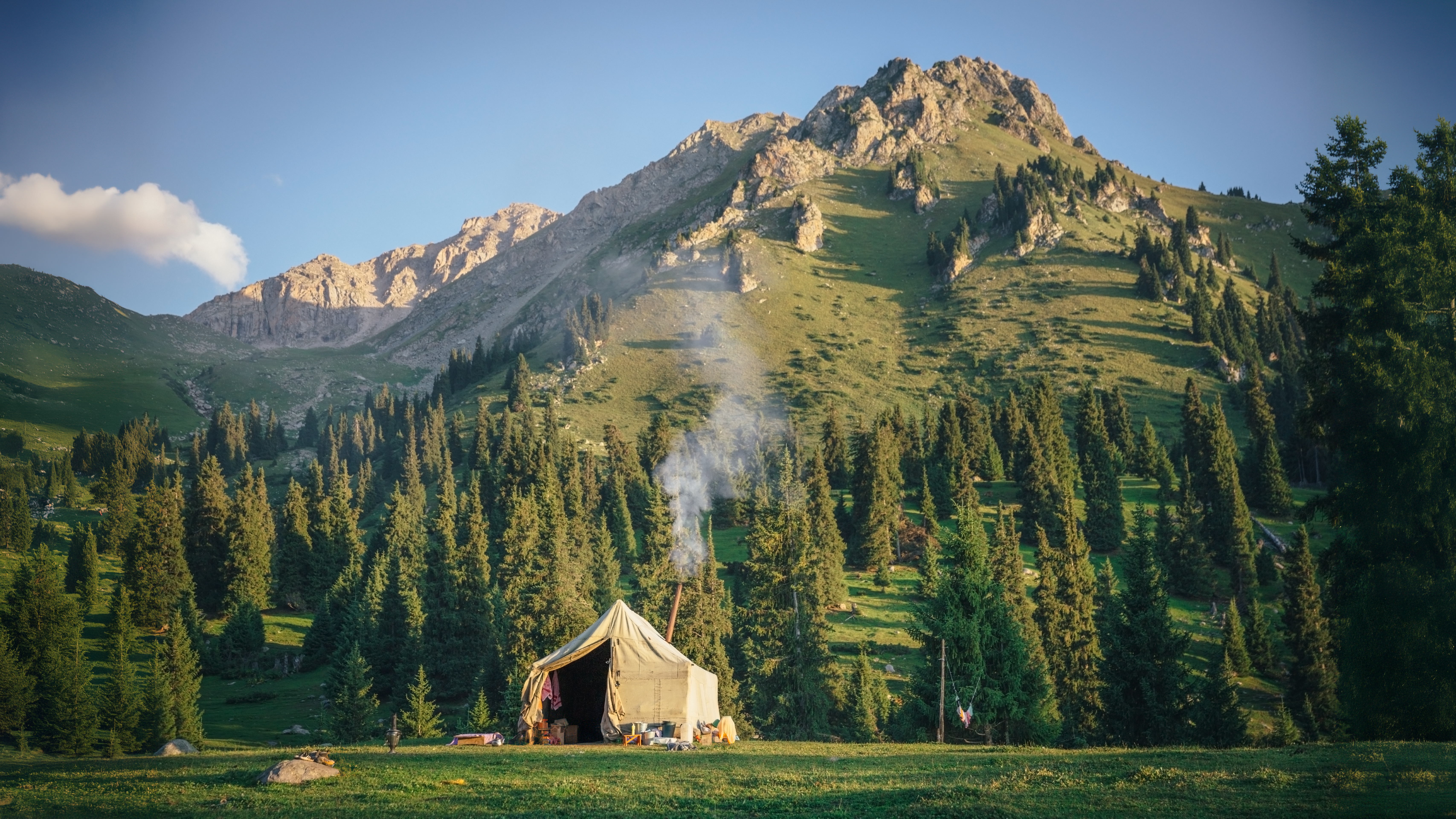 Smoke rises from a yurt set up on a field in front of the Tien Shan Mountain Range in Kyrgyzstan 