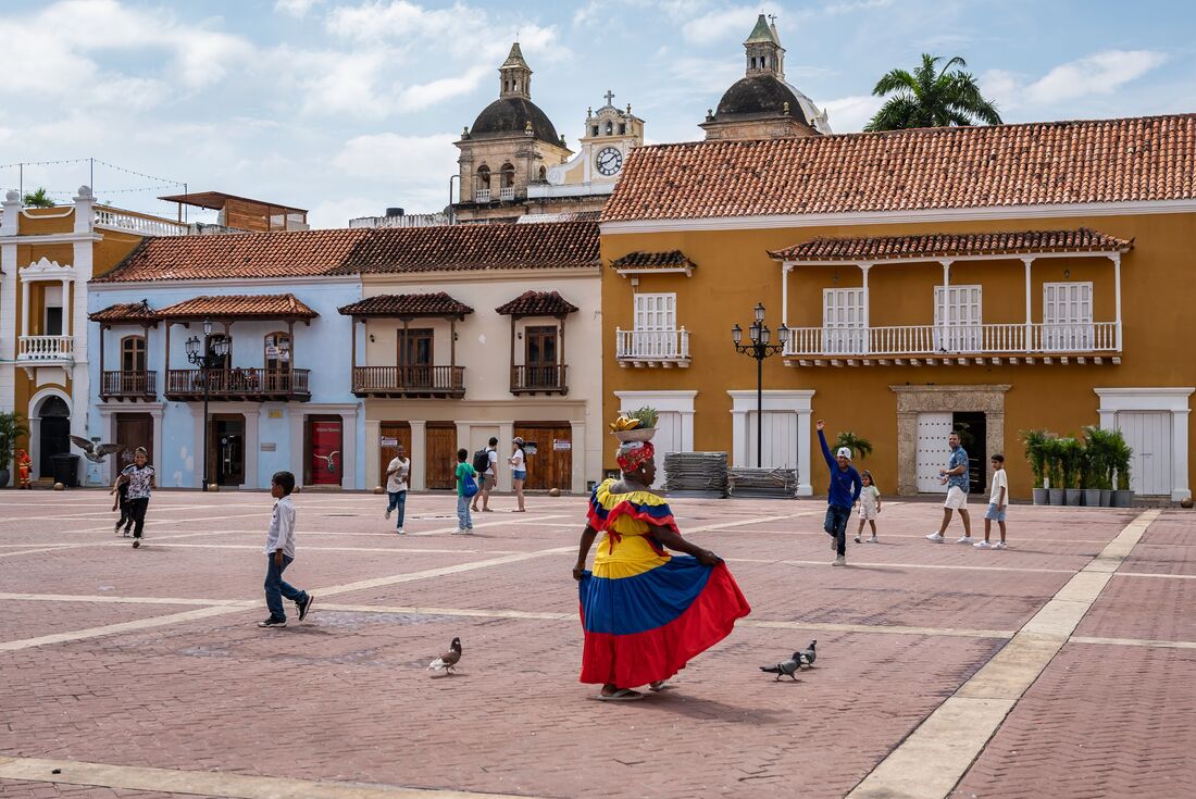 Brightly coloured dressed Palenquera selling fruit in Cartagena town square in Colombia