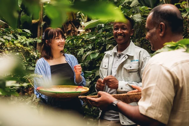 A traveller and two leaders hold baskets containing coffee beans in Tanzania