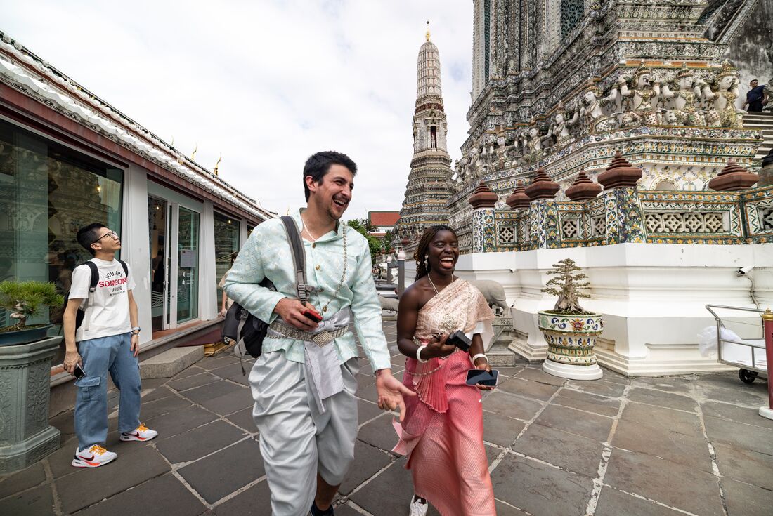 Two laughing travellers dressed in traditional Thai attire at Wat Arun, Bangkok, Thailand