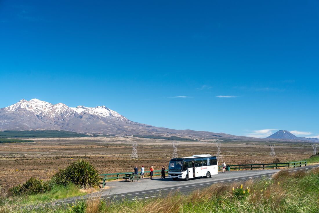 Travellers' tour bus pulled over on side of road so travellers can enjoy the view of Mount Tongariro, New Zealand
