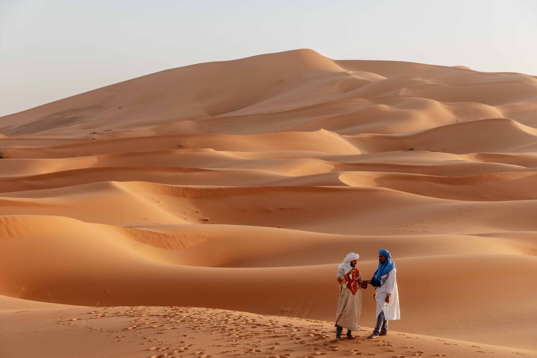 Local guides in the Sahara Desert, with vast sand dune landscape behind them, Morocco