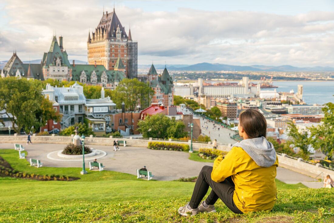 Travelling sitting on green grass, admiring the view of Chateau Frontenac Castle at Old Quebec, Canada