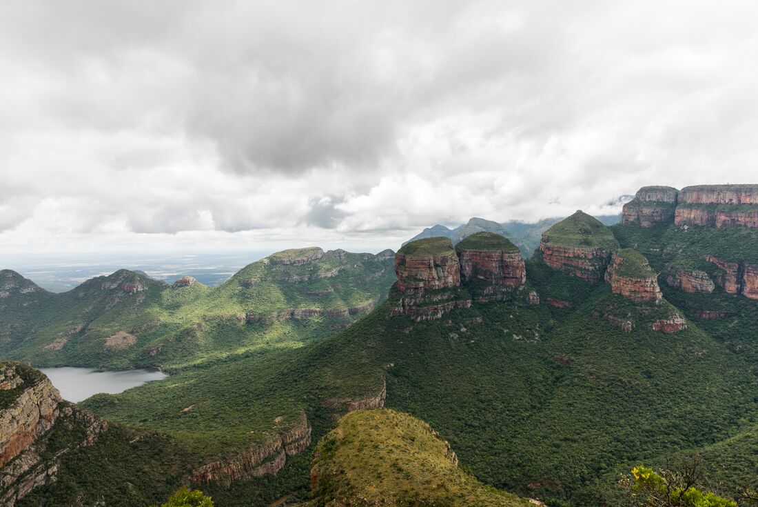 Large round stone spires seperate from a larger plateau covered in green trees rise up from a huge canyon