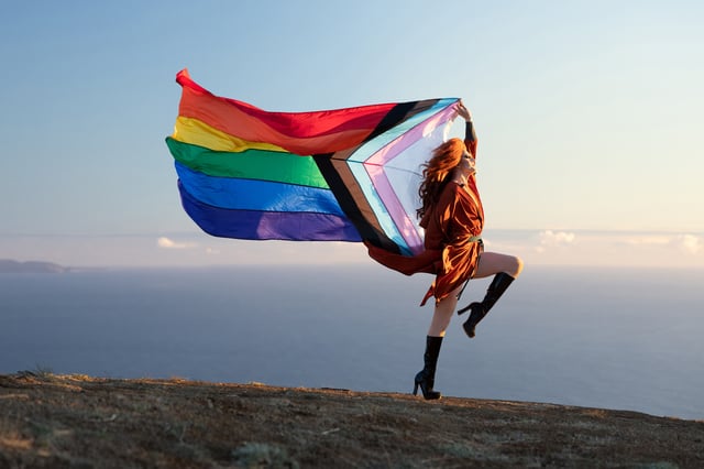 Drag queen Pattie Gonia poses outside with a colourful Pride flag