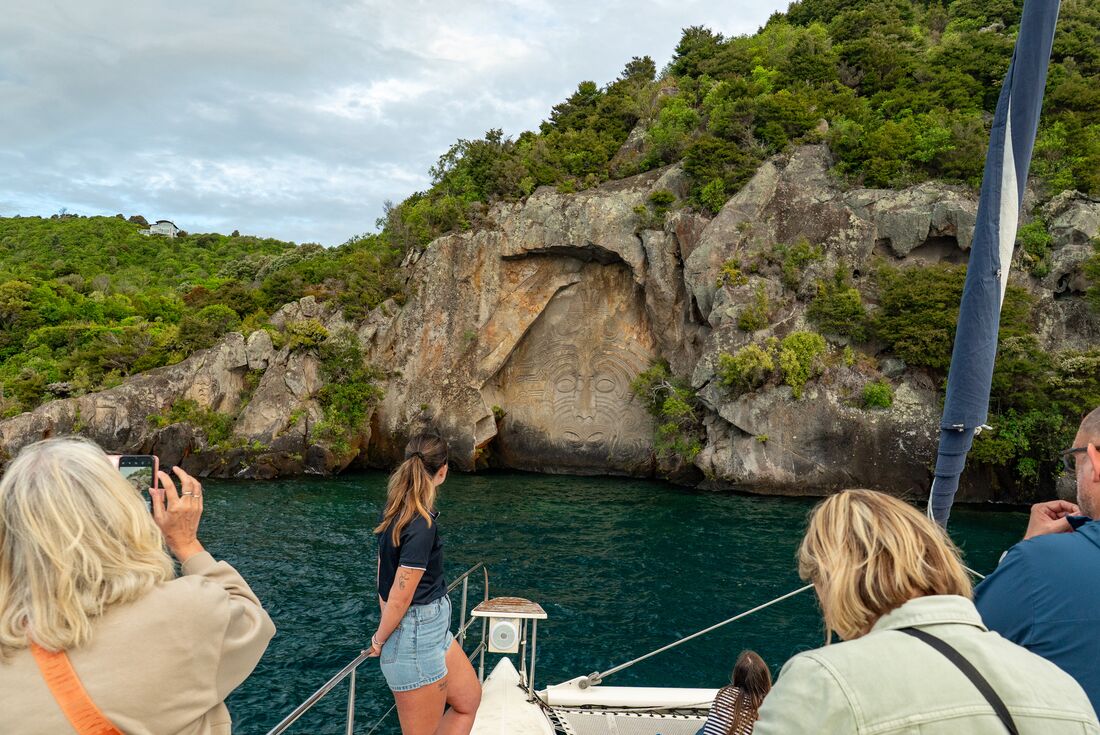 Travellers on a boat ride, viewing the Maori artwork on carved into the cliffside at Lake Taupo, New Zealand