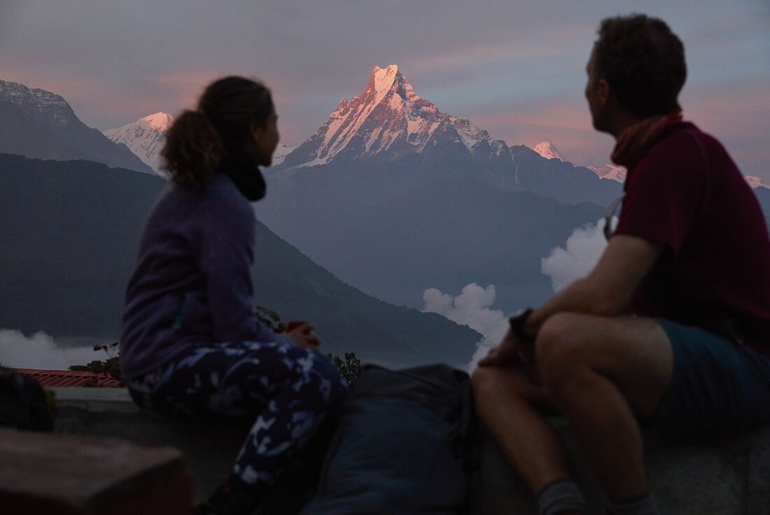 Two travellers look out from a lodge as sunrise hits a mountain in Annapurna morning in Nepal
