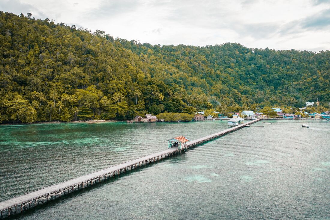 Wide view of bridge crossing the water to Yenbuba Village and mountainous forest background in Indonesia