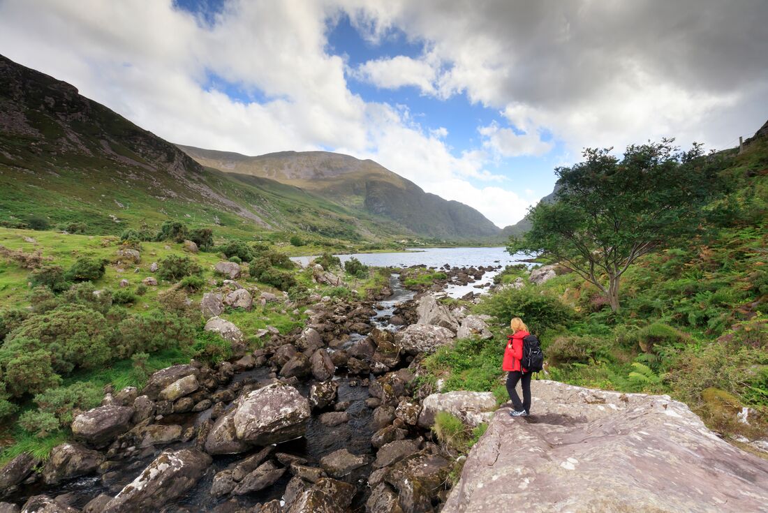 Traveller in a red jacket looking out to the distance of green grass, hills and water at Ring of Kerry, Northern Island