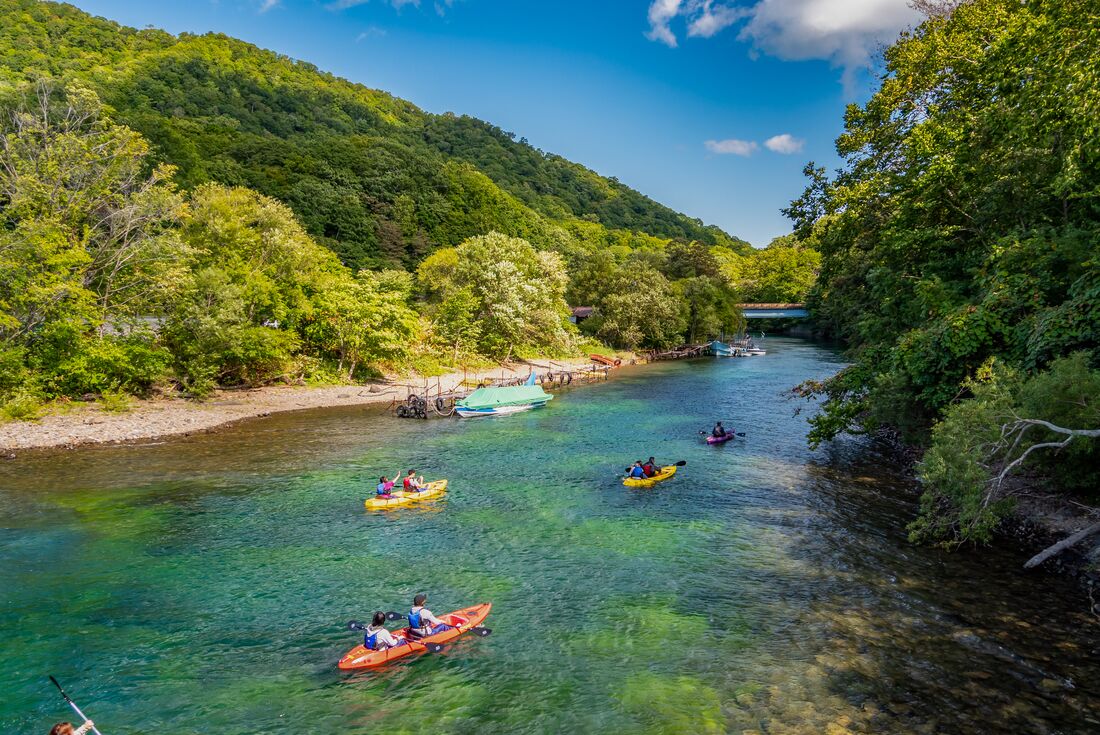 Group of travellers in double canoes row into Lake Shikotsu