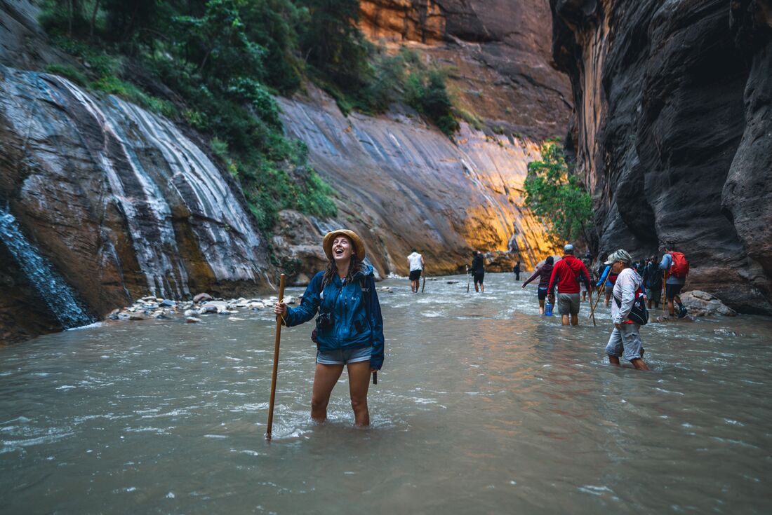Traveller stops in a river and marvels up at the majesty of Zion's cliffs as group and leader carry on hiking