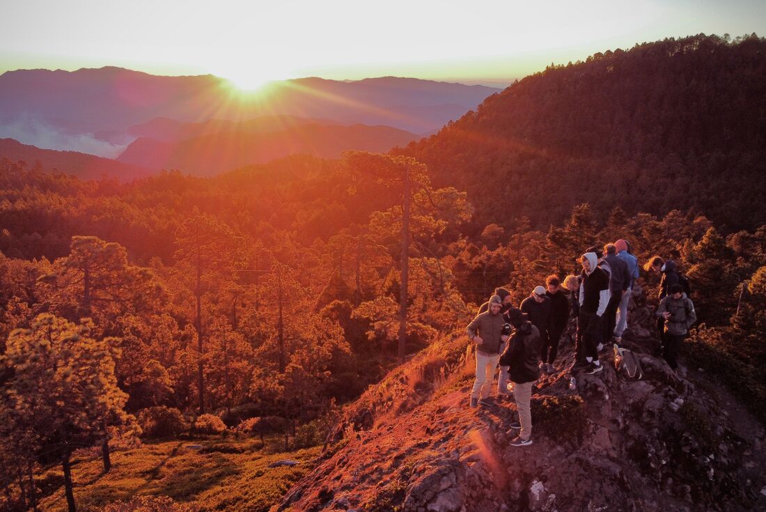 Travellers stand on a ridge looking out as dawn rises over the mountains and forests of rural Oaxaca in Mexico