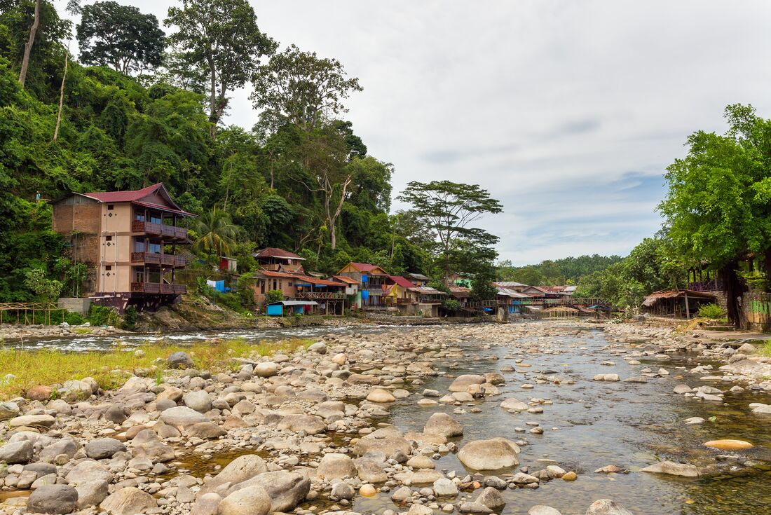 Bukit Lawawng buildings on either side of a river with forest surrounding them and mist beyond